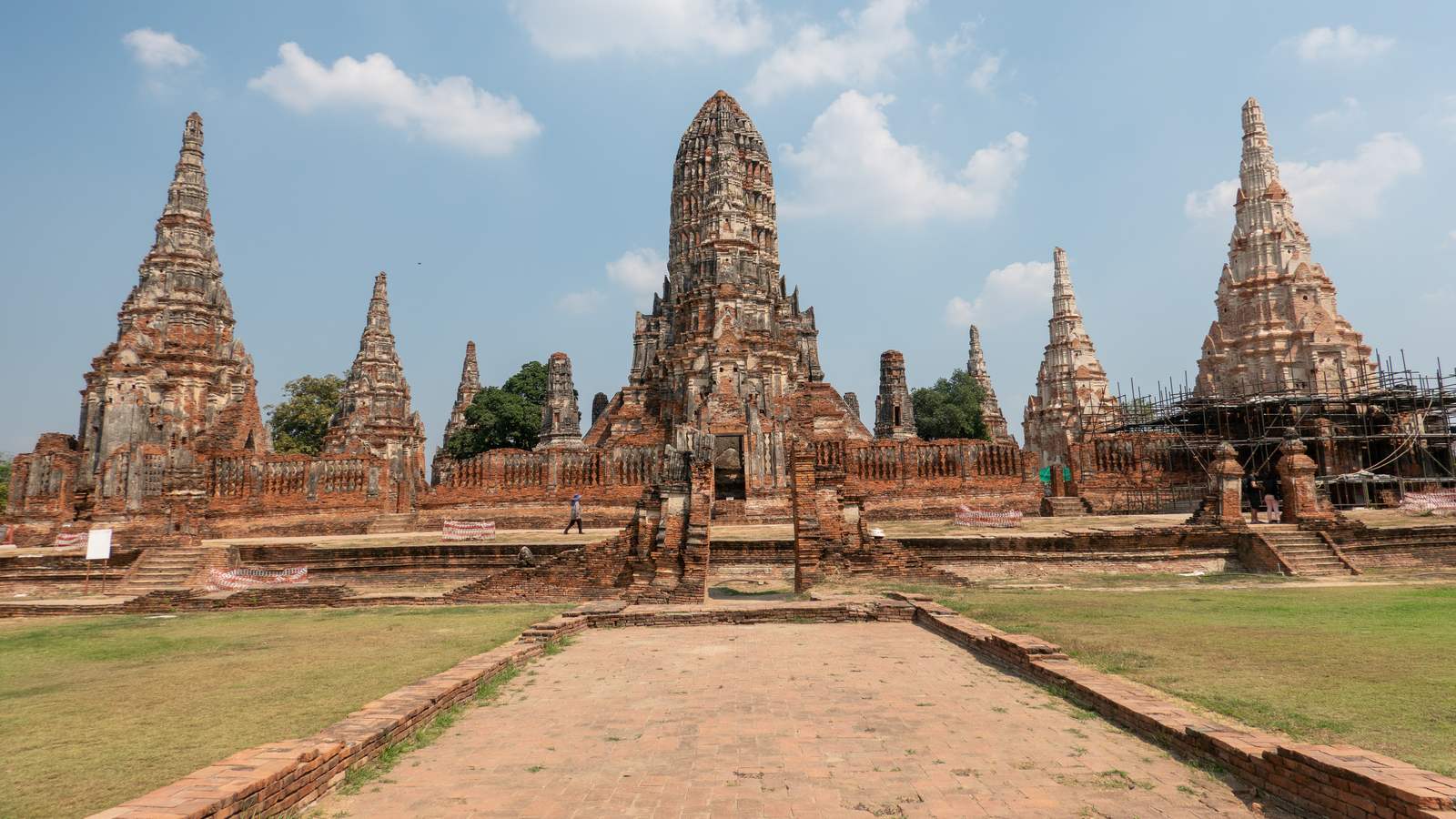 Wat Chaiwatthanaram's main Khmer-style tower and surrounding smaller towers, seen from the front brick walkway, with restoration scaffolding on the tower at right