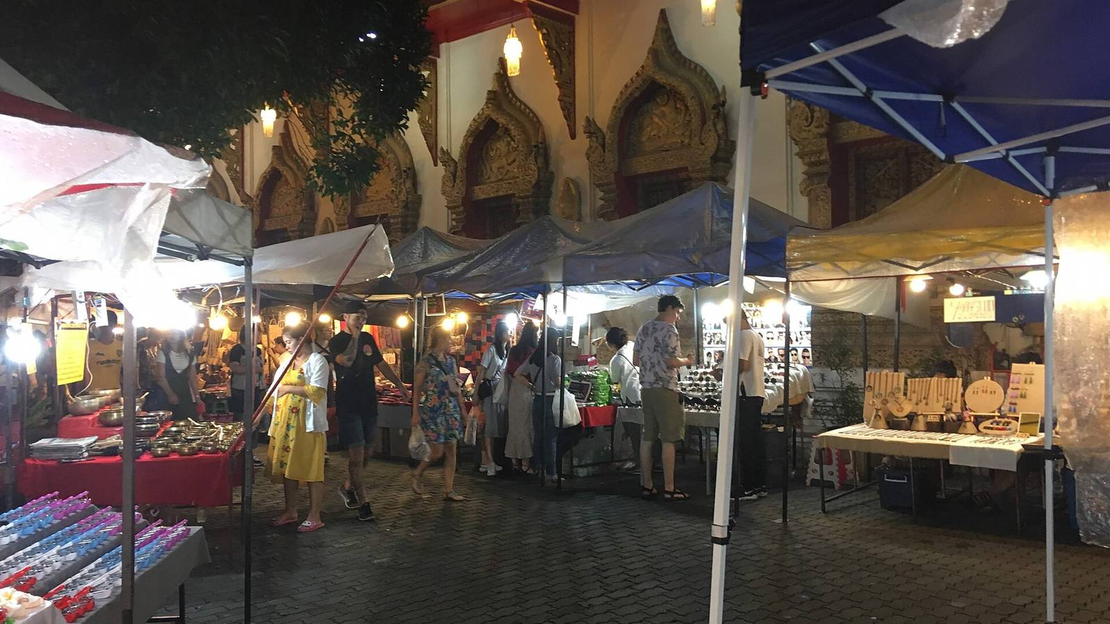 夜裡的清邁週日步行街,寺院外牆的金色雕飾下排著一列撐著遮陽棚的攤位,路上有人在逛