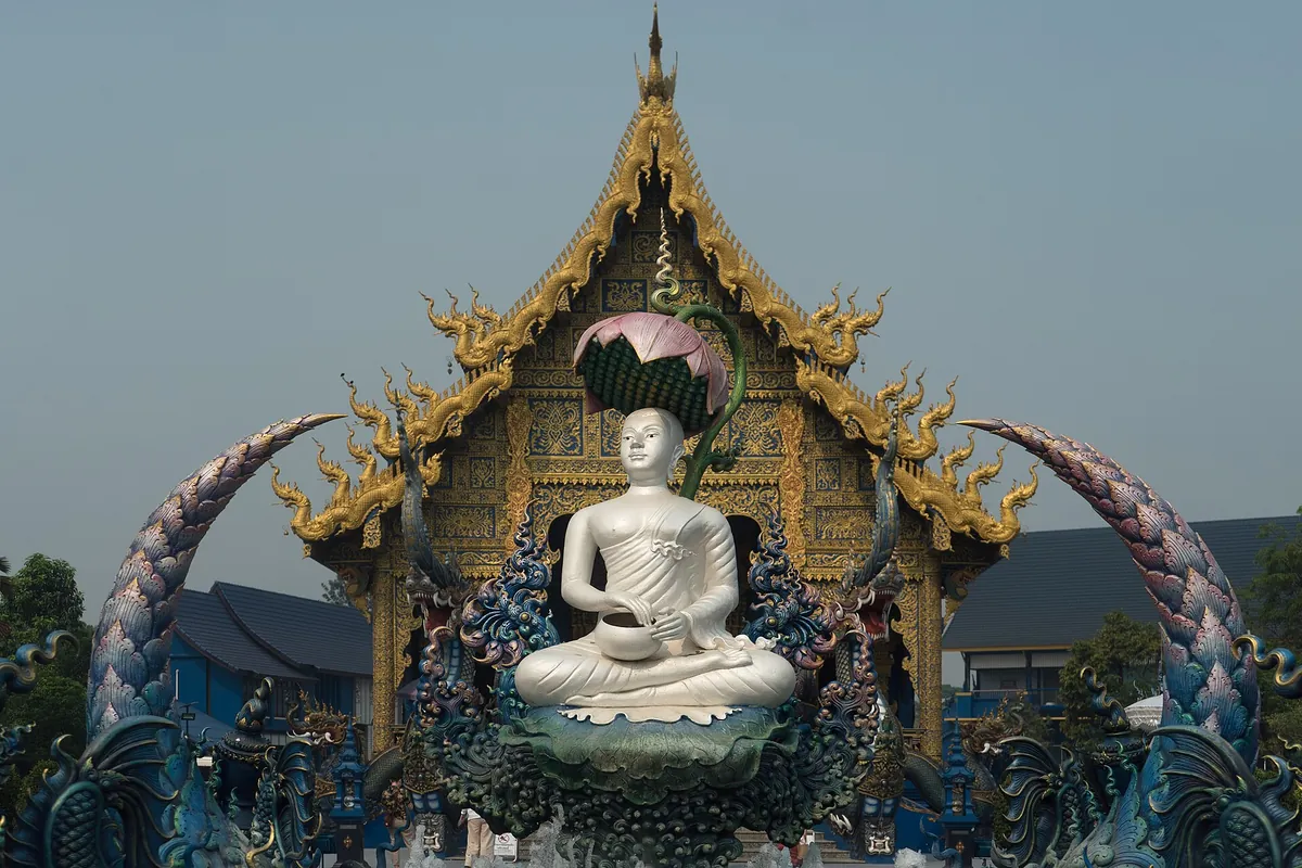 藍廟前方的白色佛像坐在蓮花座上，兩側是藍色與金色的那伽雕塑拱門，後方是金頂藍牆的大殿