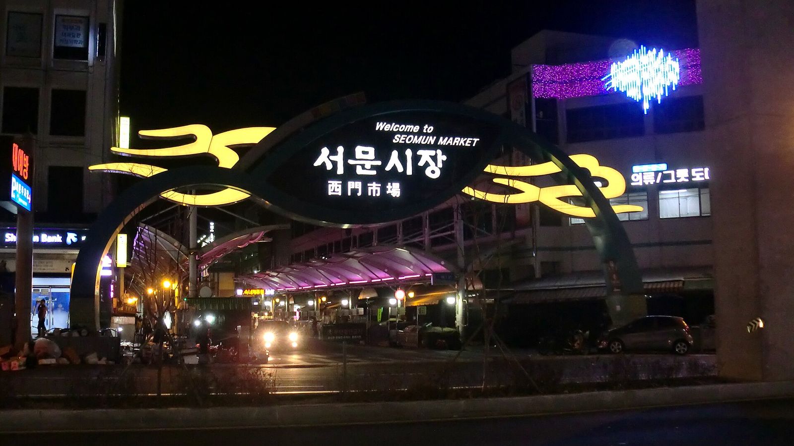 西門市場入口的夜間拱門，上面寫著서문시장與西門市場，後面是亮著燈的市場攤棚