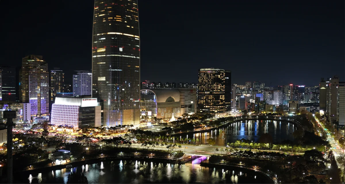 Lotte World's Magic Island at night, with the illuminated castle and rides reflected in the lake