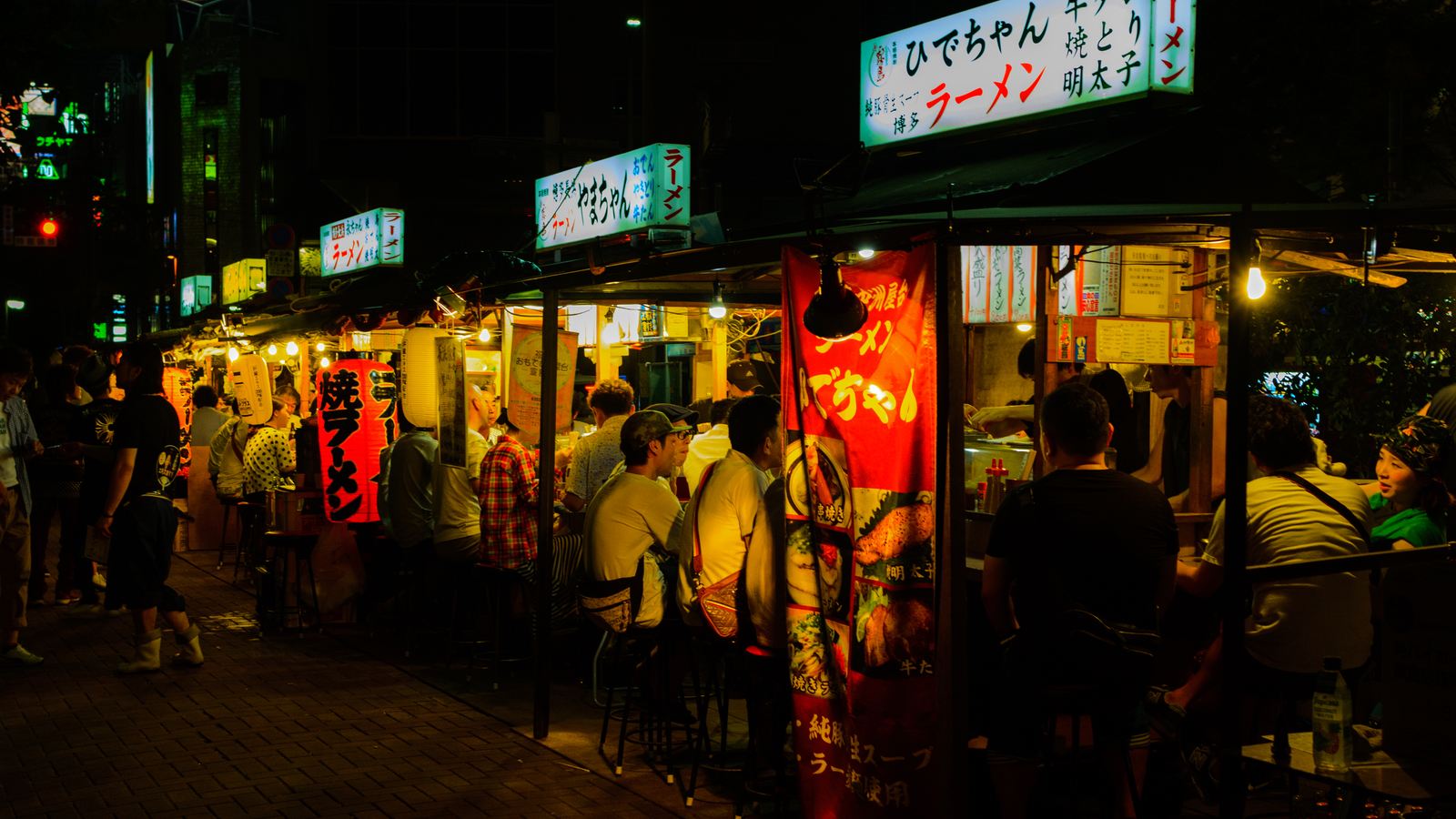 Hakata's Nakasu yatai at night, with lanterns hanging from stalls and customers seated at the counters eating ramen