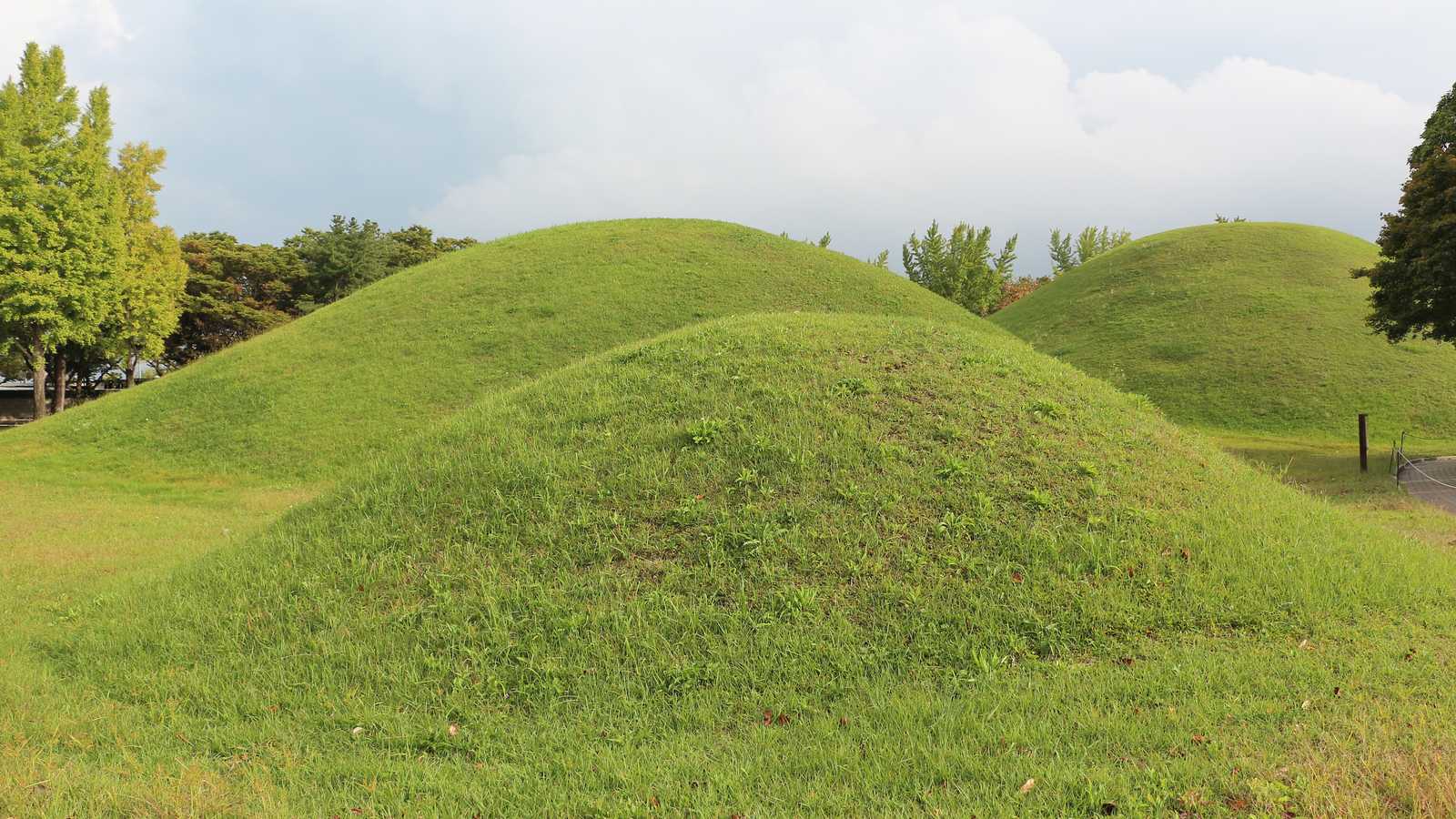 Huge grass-covered ancient burial mounds form rolling hills among scattered trees at Daereungwon in Gyeongju