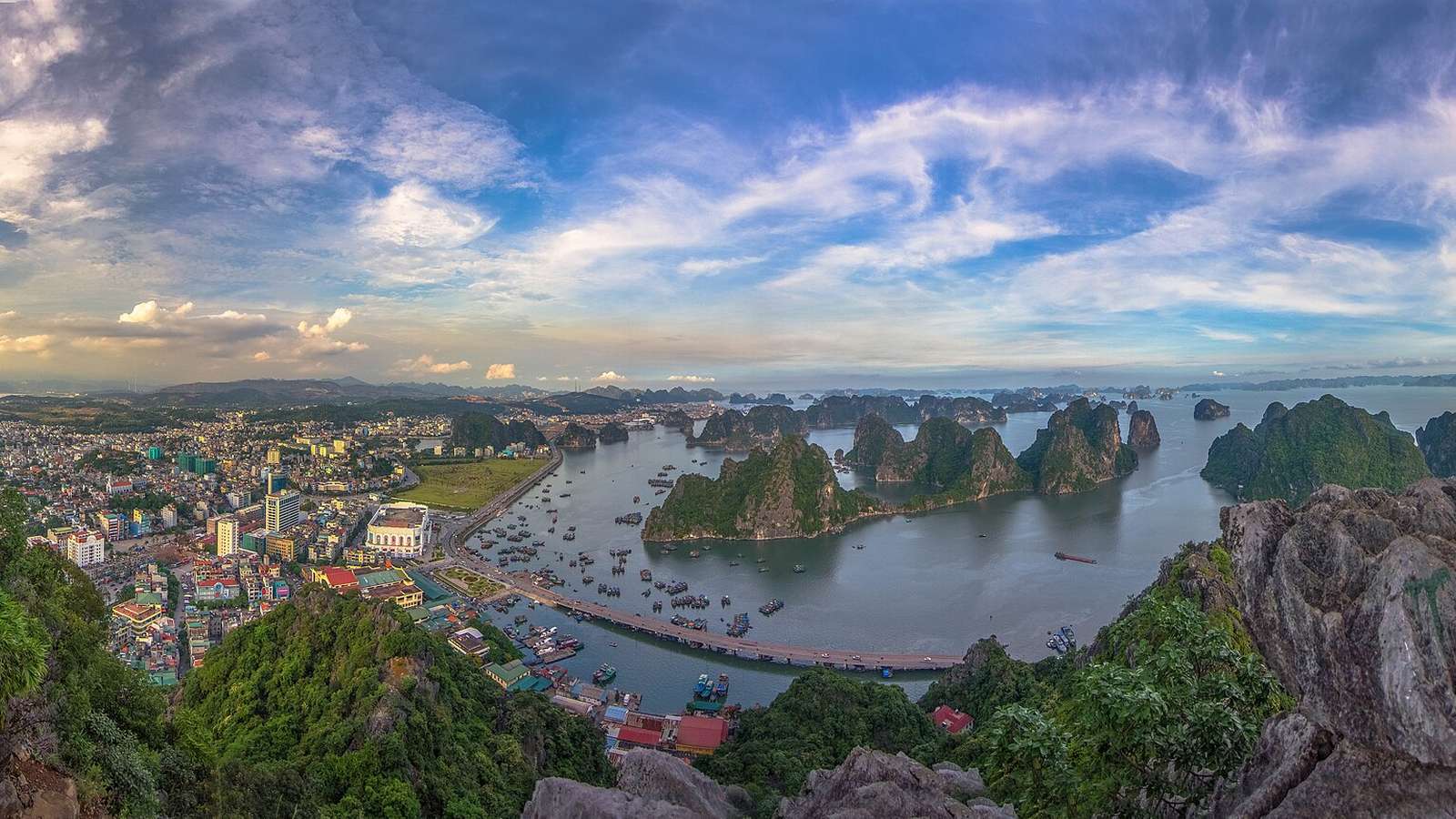 從高處俯瞰下龍市與下龍灣，市區旁的碼頭停滿船，海面上散布著石灰岩島