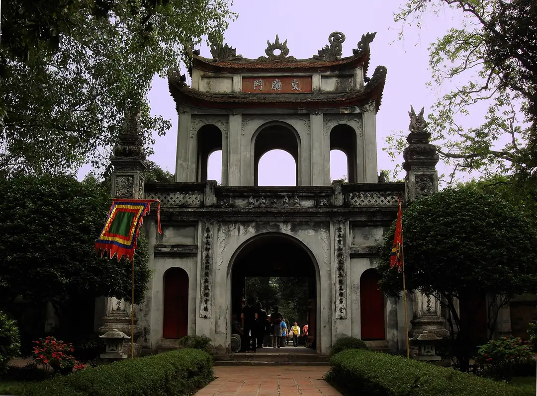河內文廟入口的三拱牌樓門，門上掛著文廟門匾額，兩側是綠樹與花叢