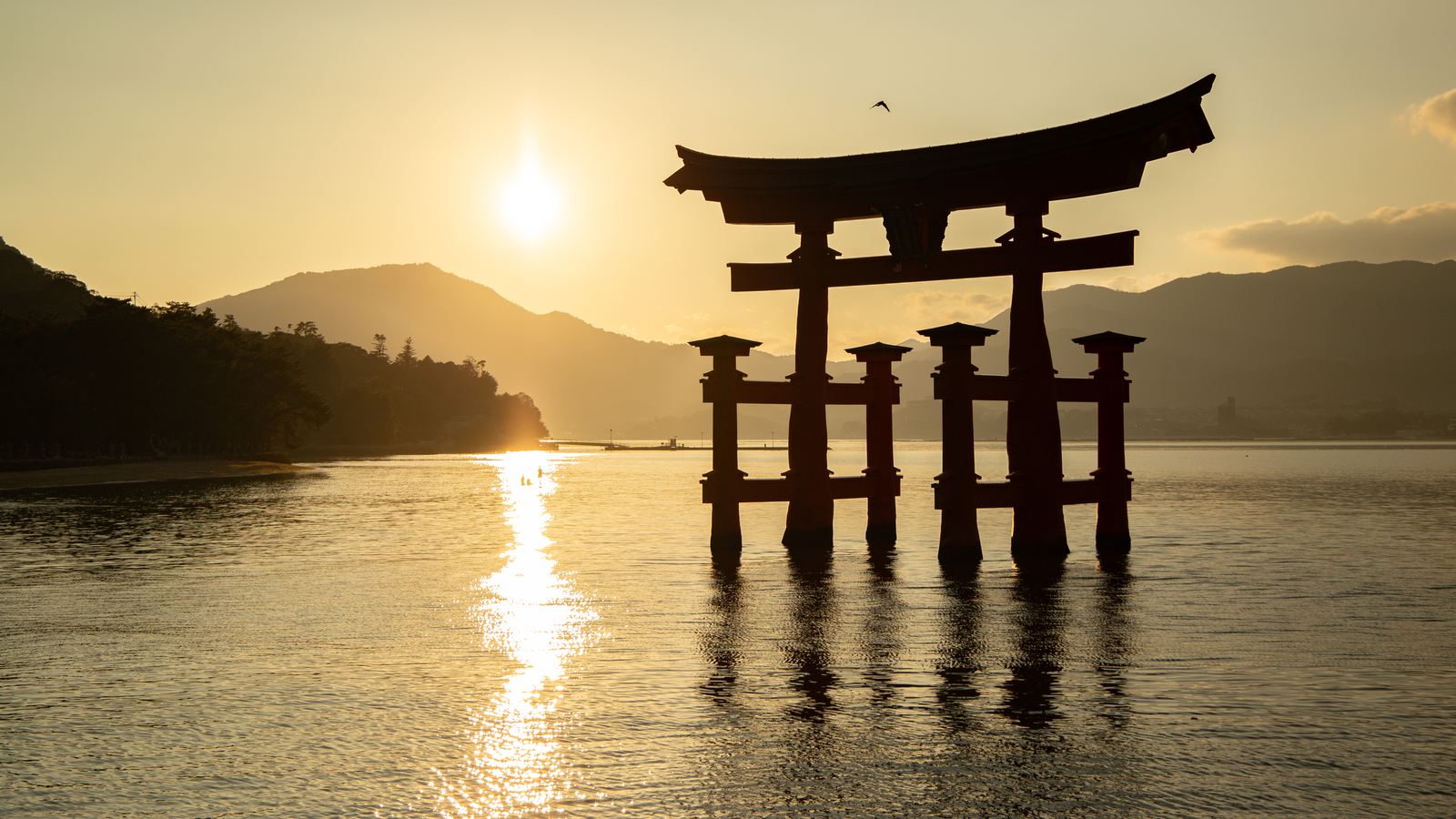 夕陽下嚴島神社的朱紅色大鳥居立在海水中，遠處是宮島的山影