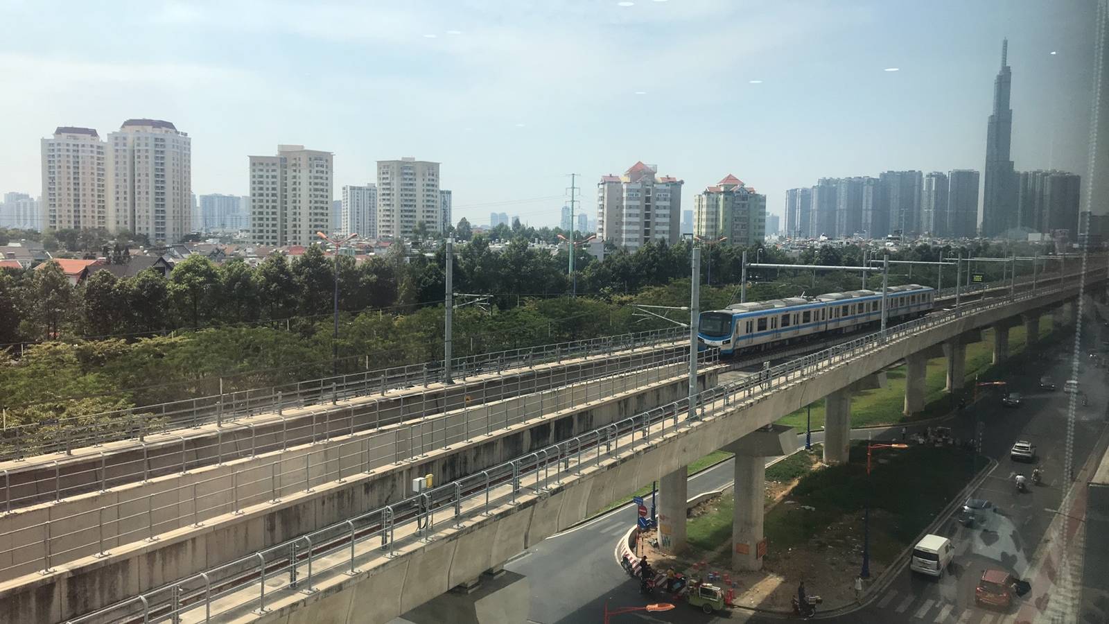 胡志明市地鐵 1 號線列車行駛在草田一帶的高架軌道上，背景是住宅大樓與 Landmark 81 高樓