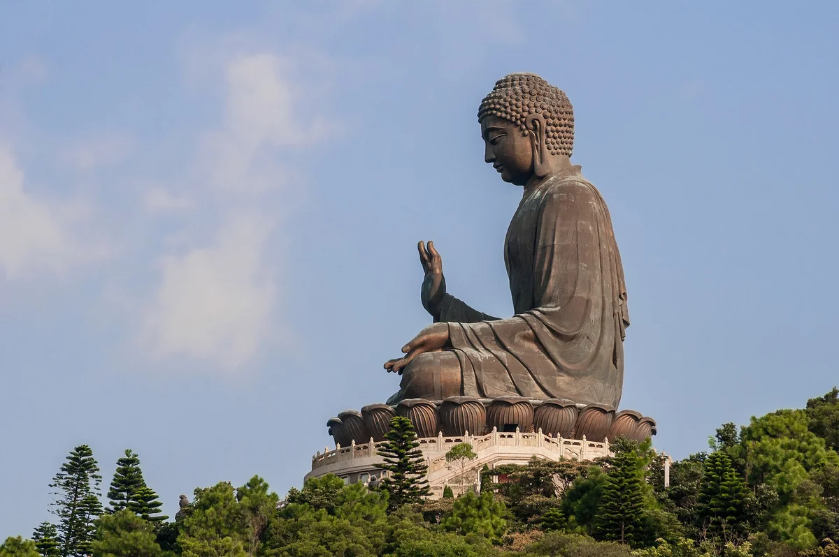 天壇大佛坐在昂坪山頂的蓮花座上，下方是綠樹，背景是藍天