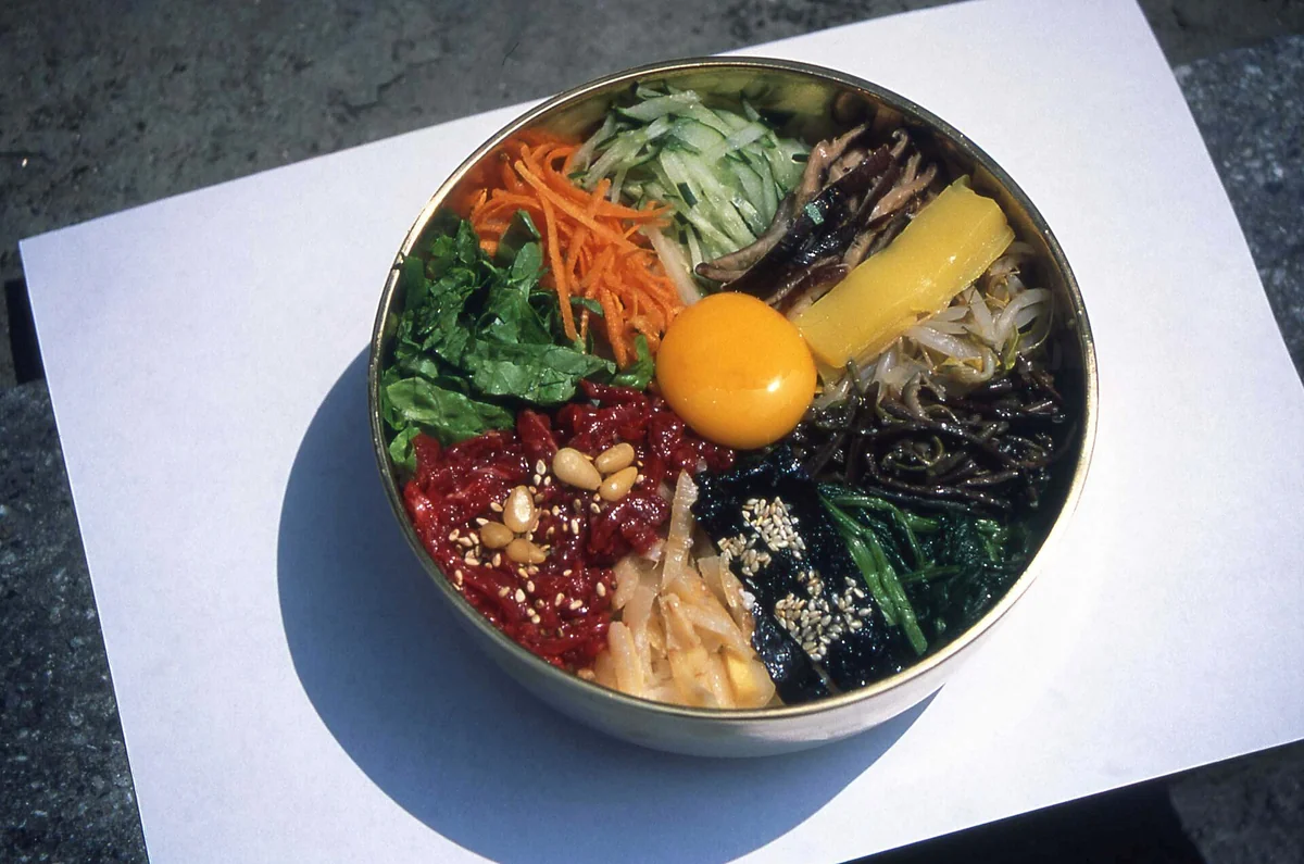一碗尚未拌勻的拌飯，蔬菜、牛肉與雞蛋分開排在飯上