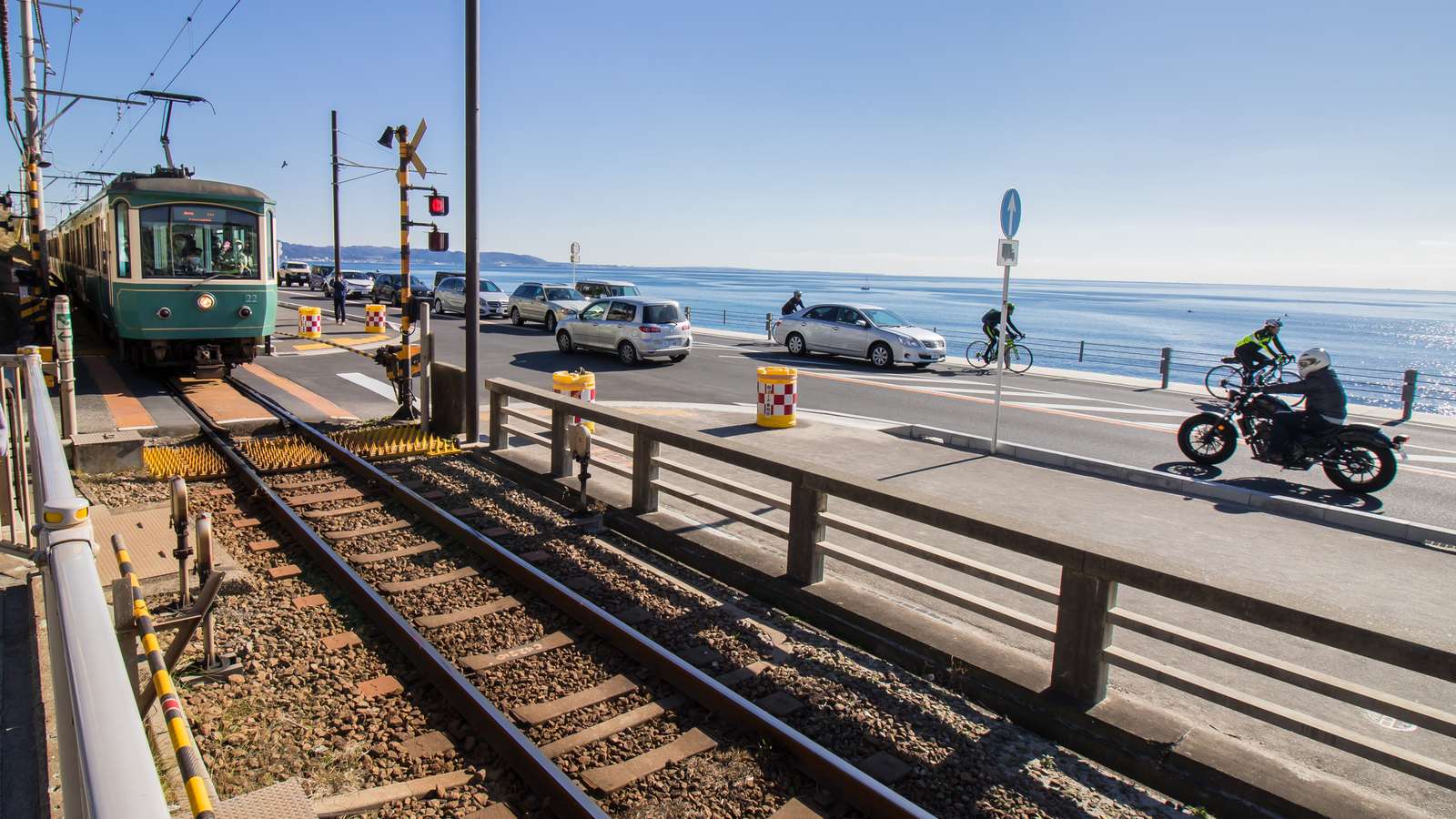 江之電列車行駛在湘南海岸旁的軌道上，遠方是七里濱的海