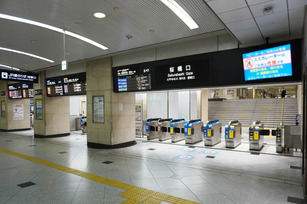 JR 大阪站櫻橋口的一排自動閘門，閘門側面貼著 IC 卡感應標示，上方是列車資訊看板