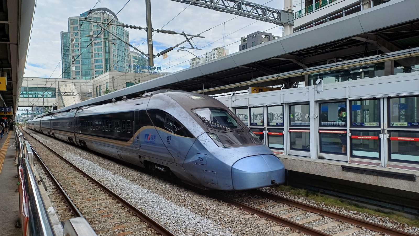 KTX-青龍高速列車停靠在月台旁，藍色流線型車頭朝向鏡頭，月台裝有安全門