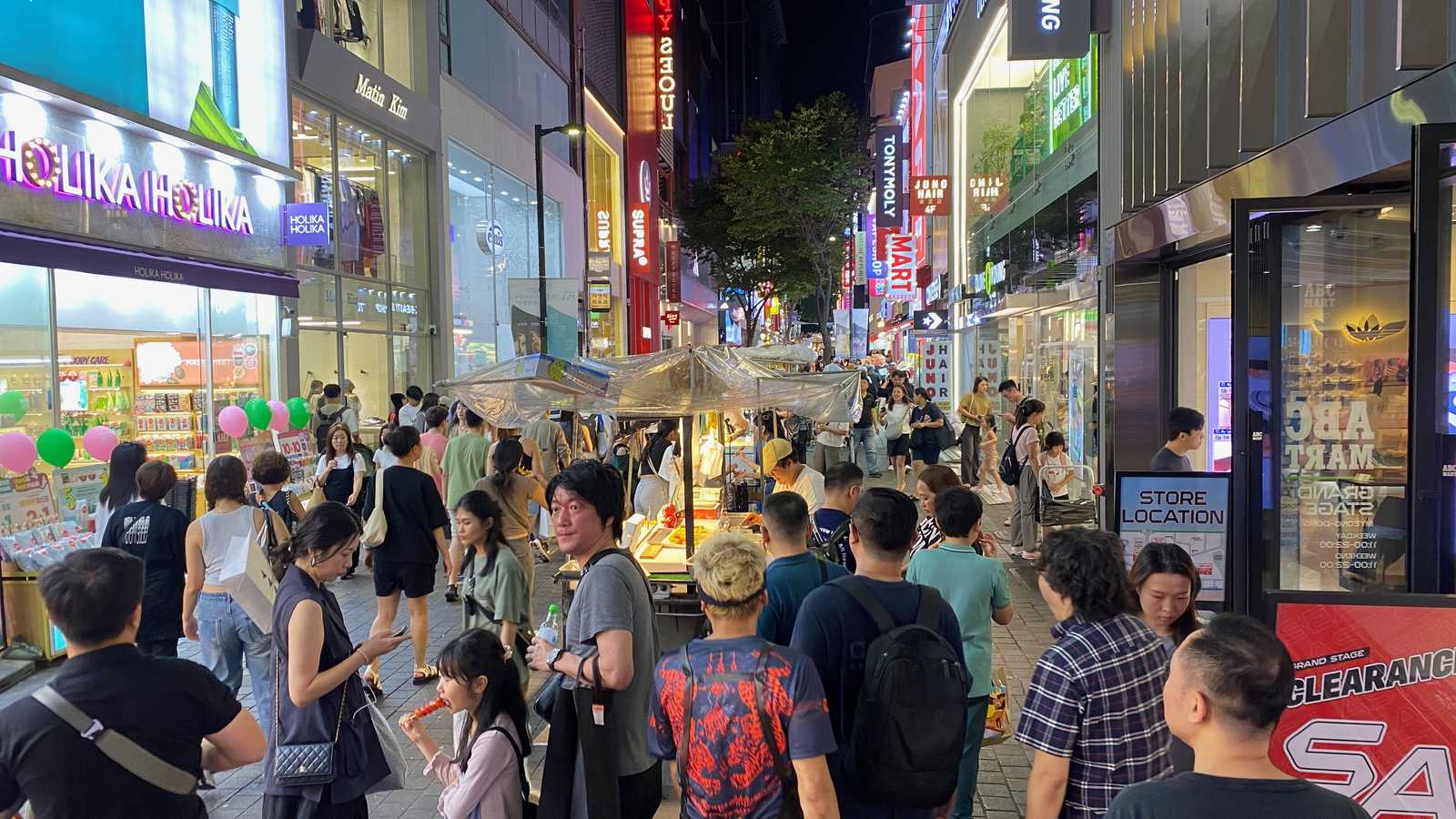 夜晚的首爾明洞街道，兩側是攤販與店家招牌，人潮往前走