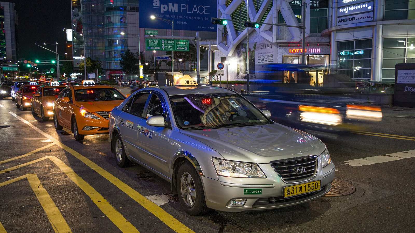 Silver and orange taxis wait for passengers at the roadside near an intersection in Seoul at night