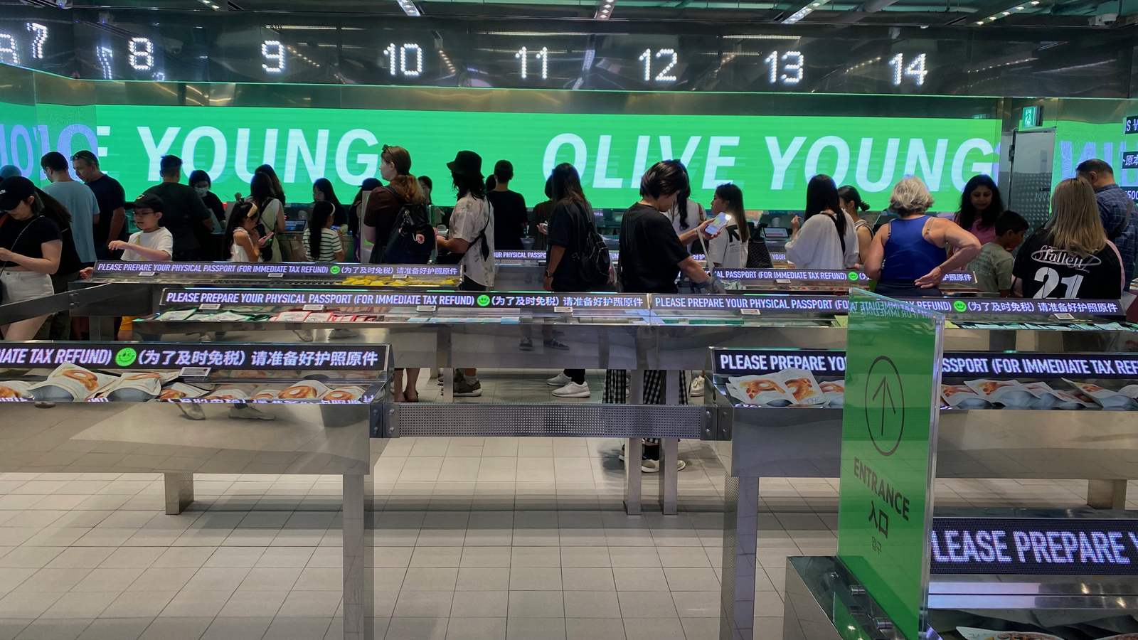 Olive Young 明洞門市的結帳櫃檯，隊伍前方的告示寫著請準備護照正本以便即時退稅
