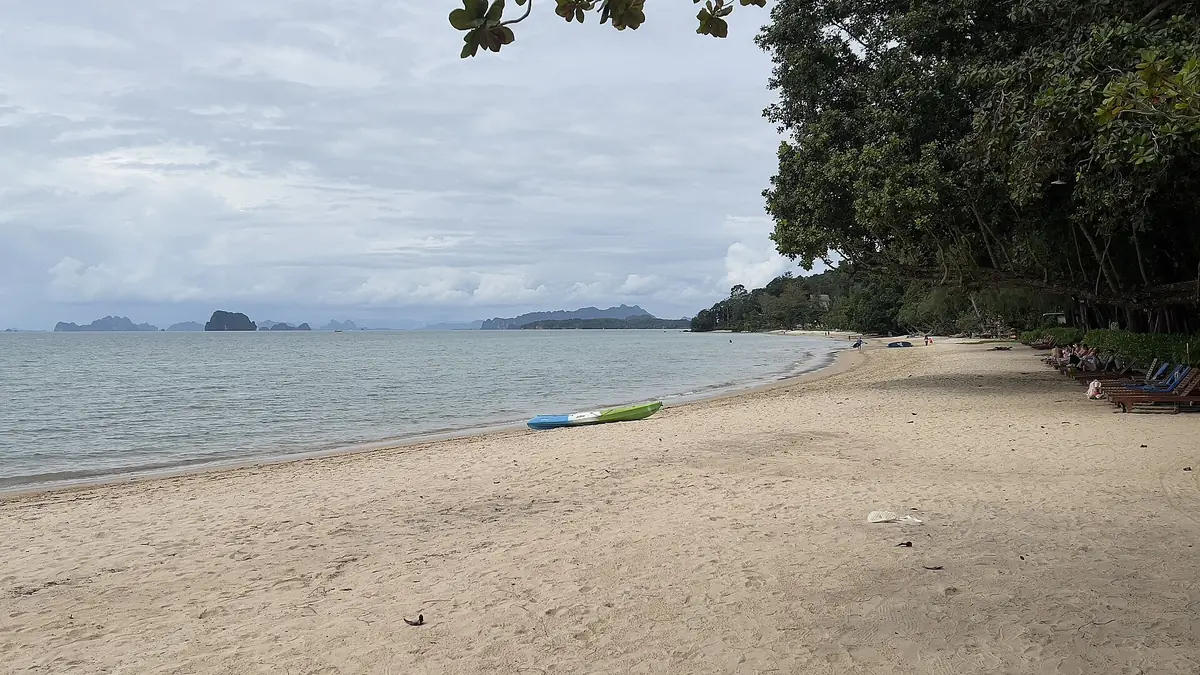Tubkaek 海灘的沙灘與平靜海面，岸邊有兩艘獨木舟，遠方是一排石灰岩島影