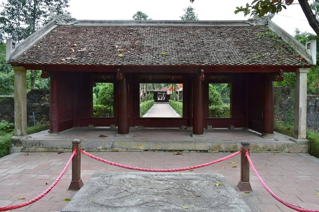 華閭古都祠廟的木造門樓，紅柱瓦頂，門前地上有一塊石雕
