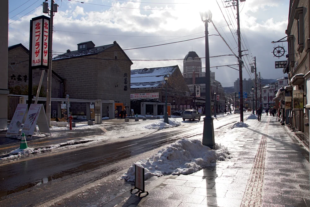 Snow and compacted ice on Otaru's Sakaimachi Street, with stone shops and a Kitaichi Glass sign