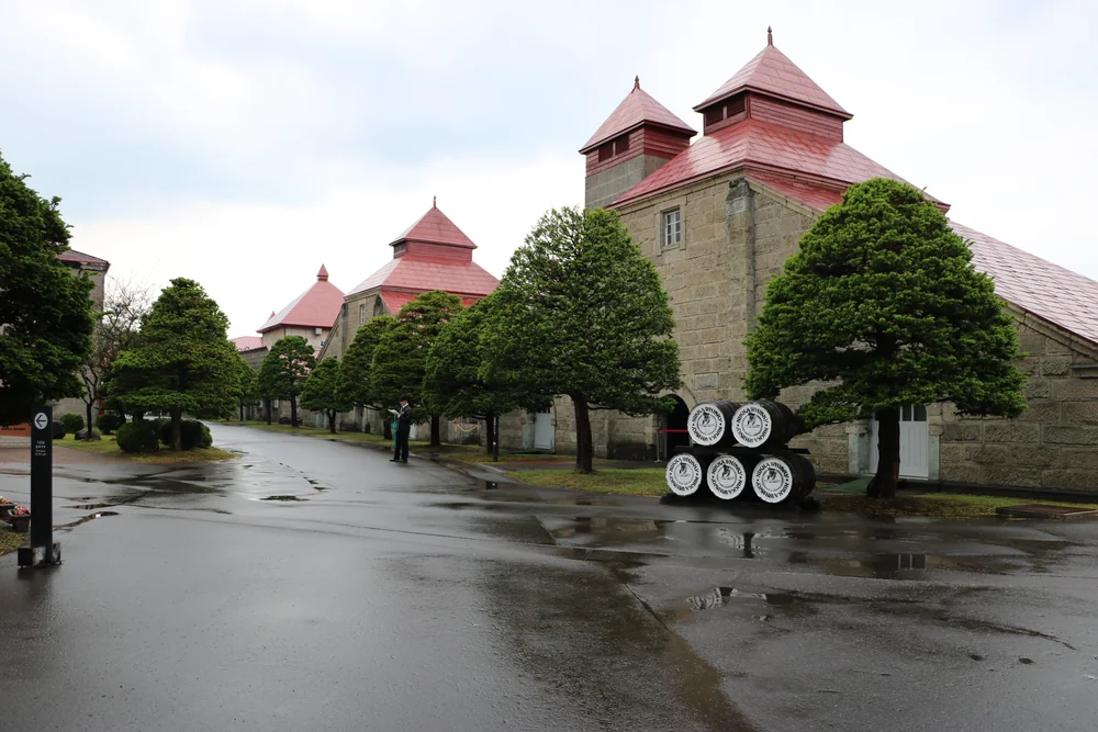Stone buildings and the red-roofed drying tower at Nikka Yoichi Distillery, with branded whisky barrels in front