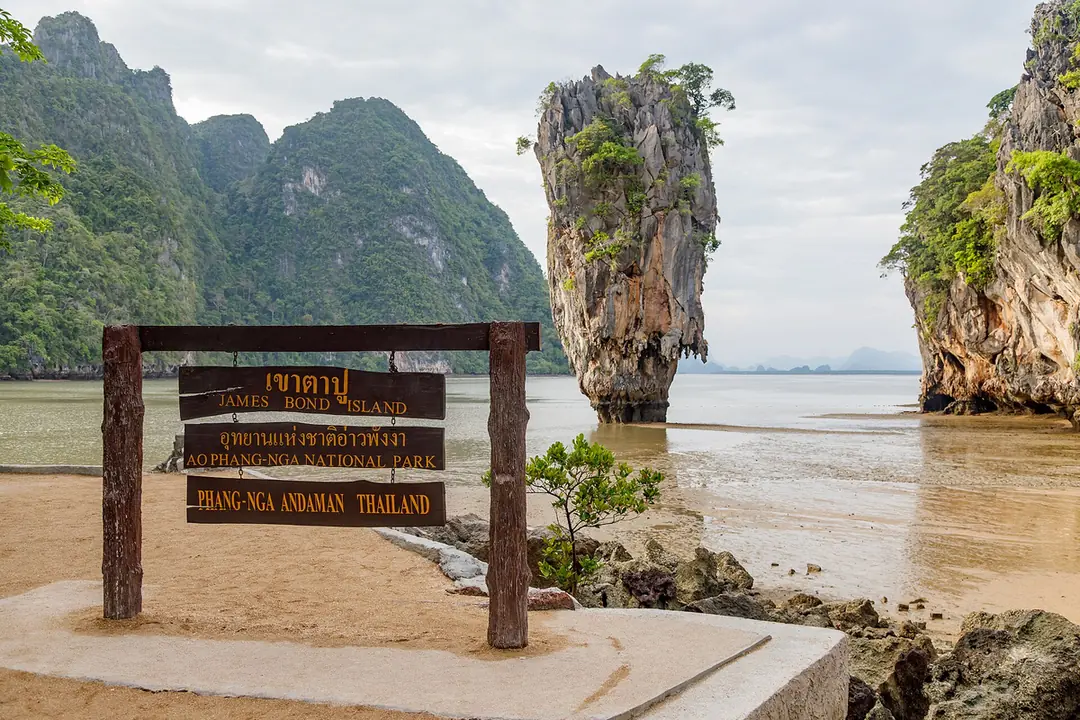 攀牙灣淺灘上的 James Bond 島孤立岩柱,前方沙灘立著寫有 James Bond Island 與 Ao Phang-nga National Park 的木牌