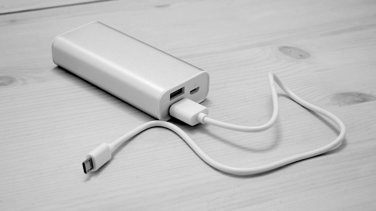 放在木桌上、插著充電線的淺色行動電源