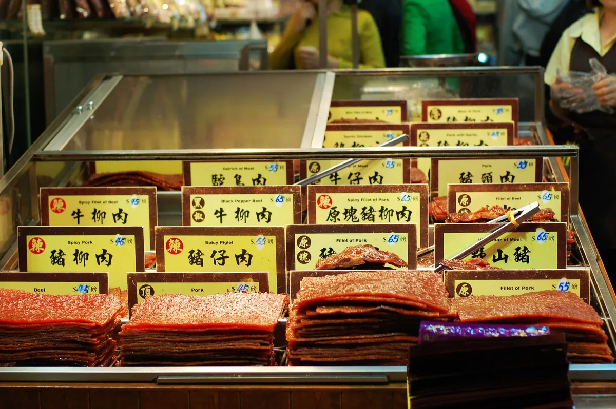 肉乾店玻璃櫃裡一疊疊的豬肉乾與牛肉乾，前面插著豬柳肉、牛柳肉等以磅計價的品名價格牌