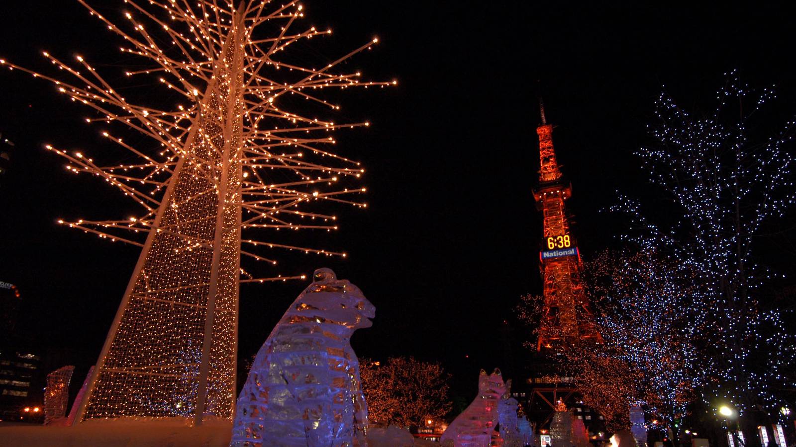 札幌雪祭大通會場夜景，打燈的冰雕與燈飾樹，後方是札幌電視塔