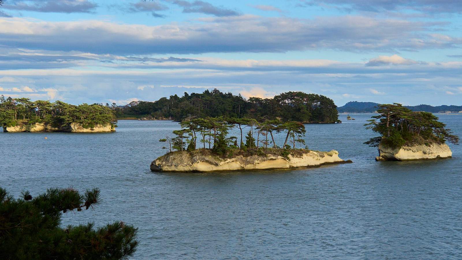 松島灣上長著松樹的幾座小岩島，海面平靜，遠處是海岸線與雲層