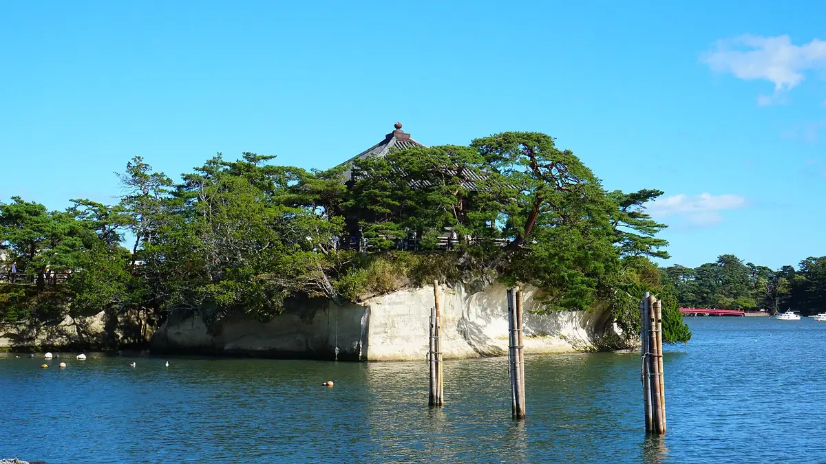 松島灣上的五大堂，堂宇立在長著松樹的小岩島上，遠處可以看到朱紅色的福浦橋