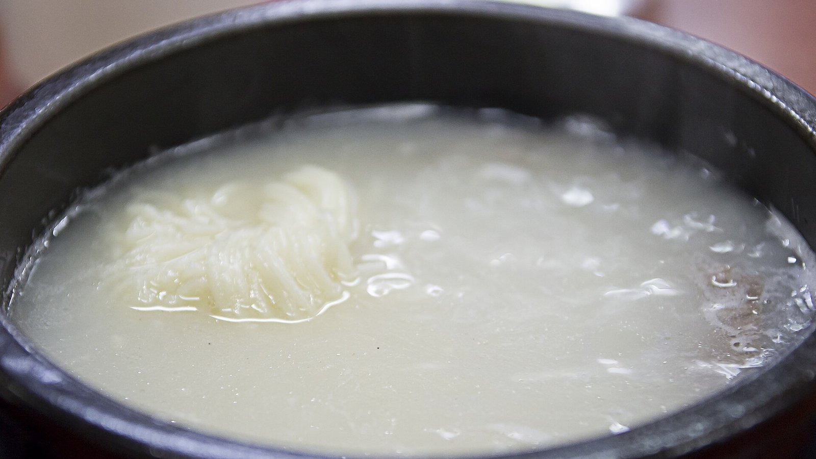 深色厚壁湯碗裝著雪濃湯，左側湯面上有一把捲起的細麵，其餘湯面看不到明顯配料