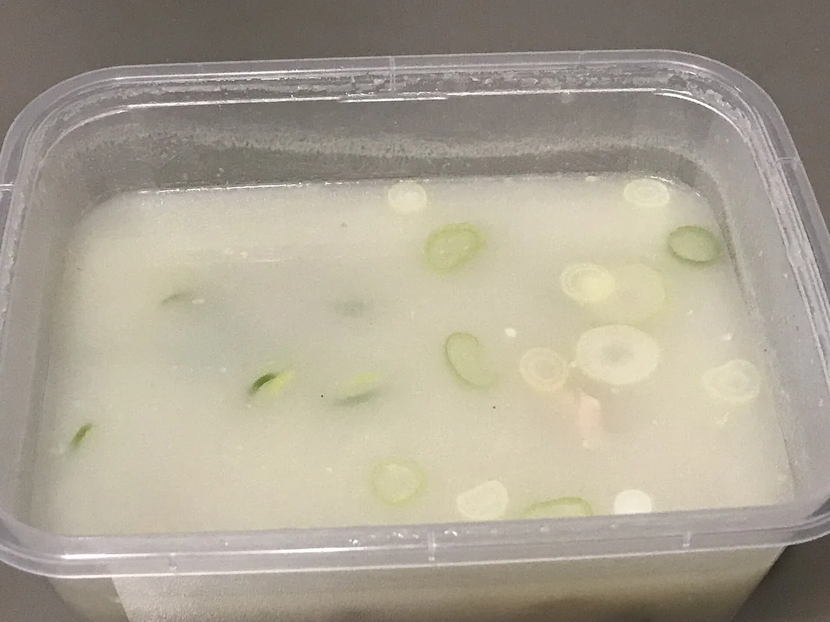 一個外帶盒裝著牛骨湯，湯面上飄著切片蔥花，隱約看得到一點配料