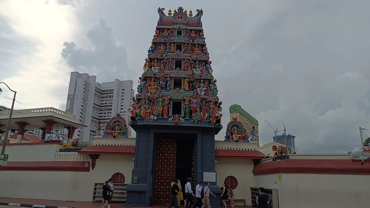 Colourful entrance tower of Sri Mariamman Temple, layered with statues, with pedestrians walking past