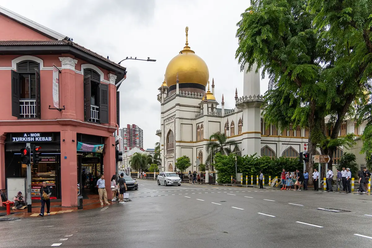 Golden dome and white minaret of Sultan Mosque seen from a Kampong Glam street corner, with a pink historic shophouse to the left