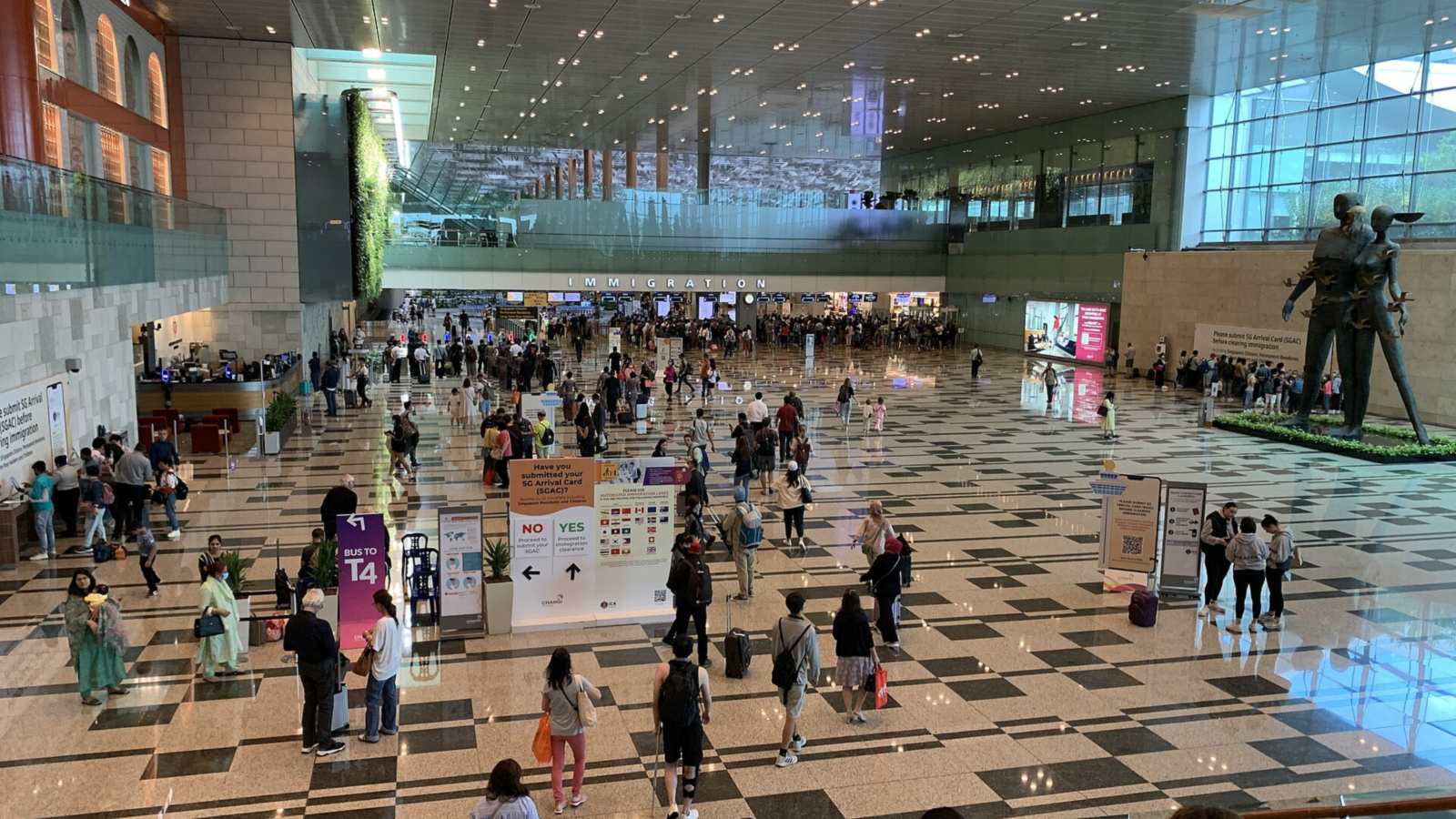 樟宜機場第三航廈入境大廳，旅客拖著行李走向遠處寫著 IMMIGRATION 的入境審查區，前方立牌問旅客是否已送出 SG Arrival Card，分成 NO 與 YES 兩個方向