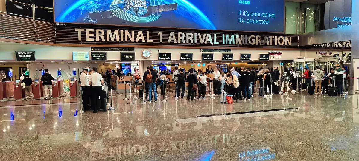 樟宜機場第一航廈入境審查區，上方招牌寫著 TERMINAL 1 ARRIVAL IMMIGRATION，左側是自動通關閘門，右側旅客在人工櫃檯前排隊