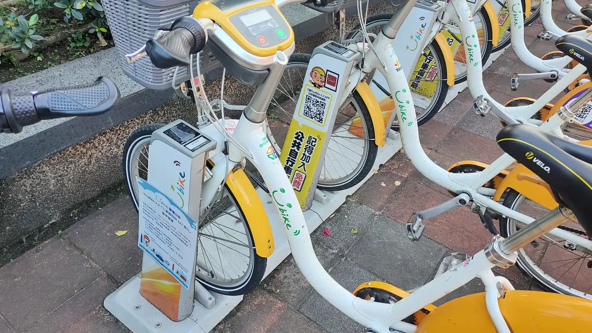 YouBike 2.0 bikes locked into docks; a yellow sign on a dock post shows a QR code and the words 記得加入公共自行車傷害險 免費