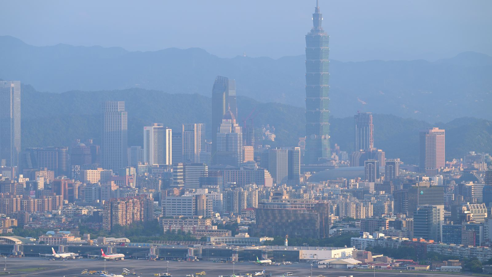 Taipei skyline with Taipei 101 rising behind rows of city buildings and the apron of Songshan Airport in the foreground