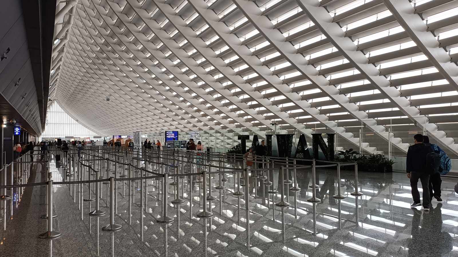 Immigration queue lanes and a large TAIWAN sign under the lattice roof of Taoyuan Airport Terminal 1 arrivals