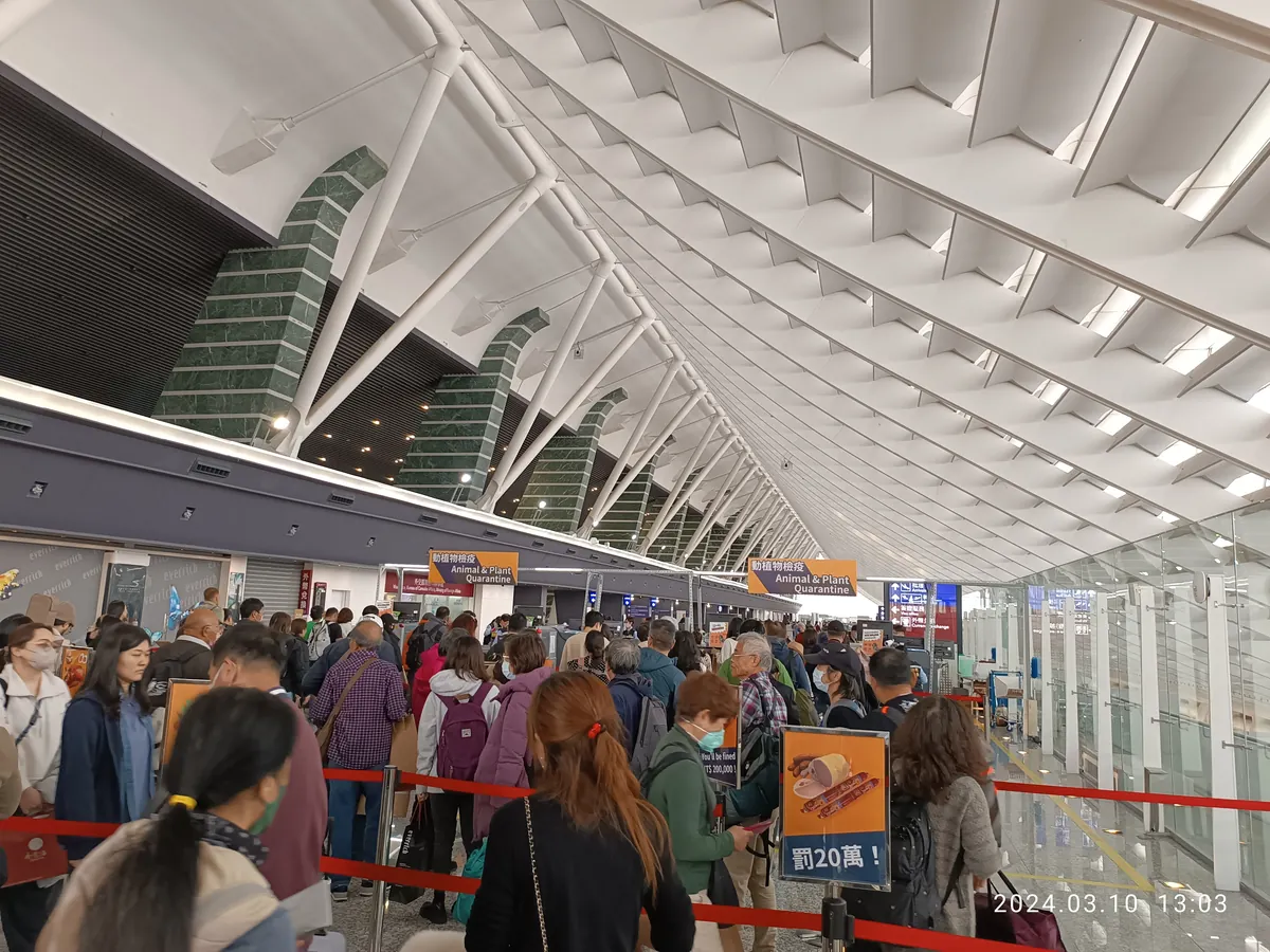 Arrivals queue under Animal and Plant Quarantine signs at Taoyuan Airport Terminal 1, with a poster warning of a NT$200,000 fine for meat
