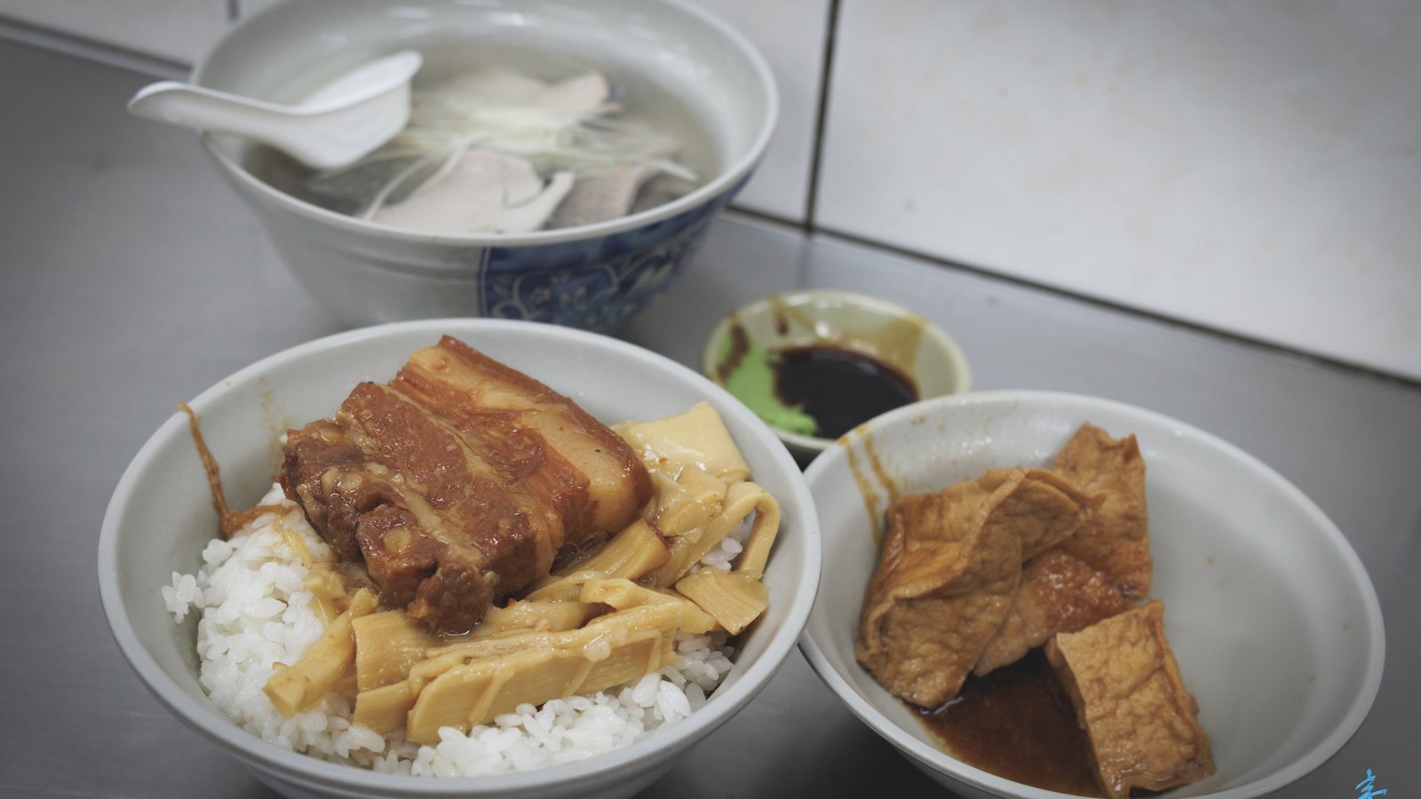 Braised pork belly rice with bamboo shoots, braised fried tofu and a bowl of milkfish skin soup on a steel counter