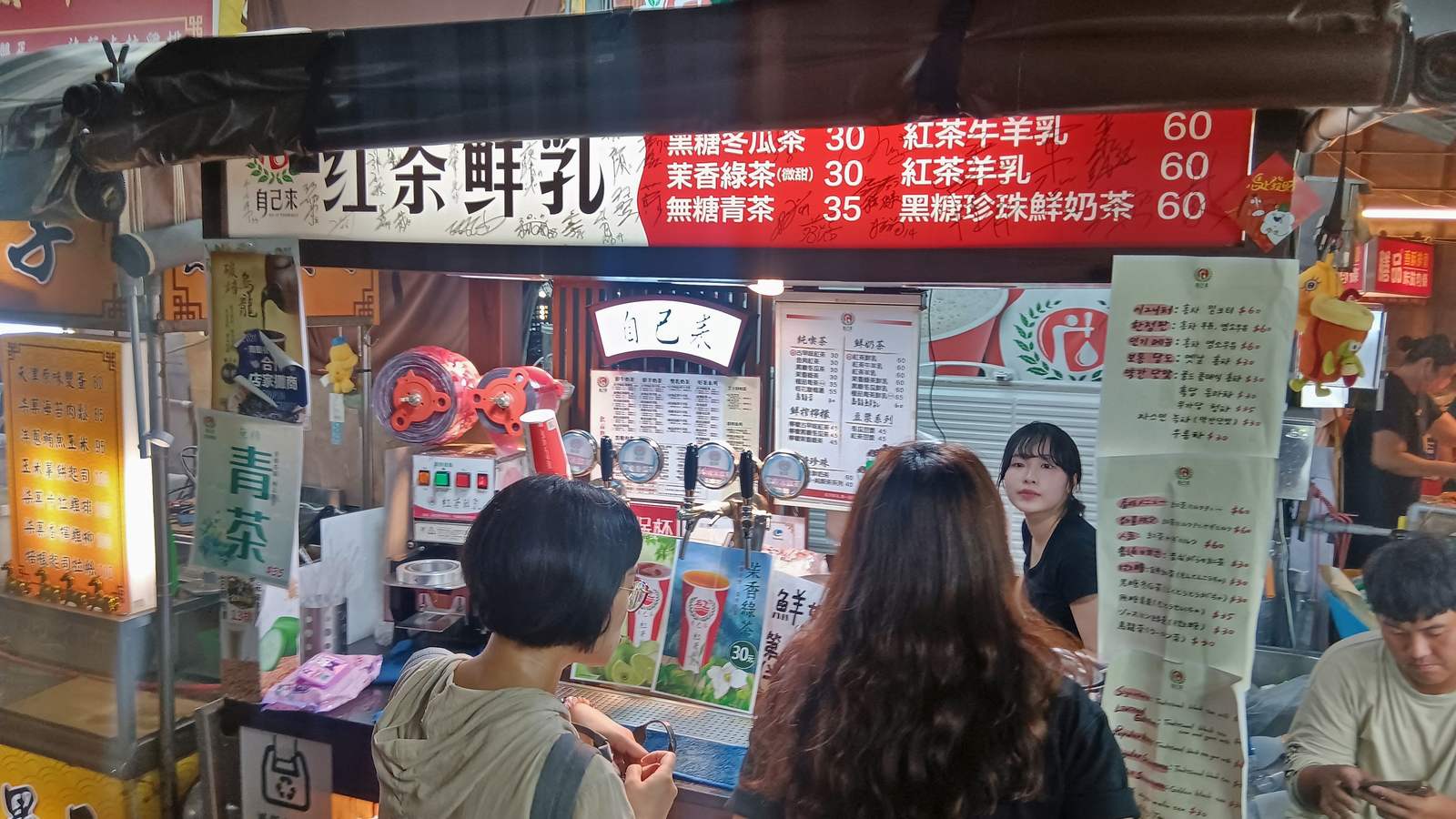Customers ordering at a drinks stall with a red price board at Ruifeng Night Market in Kaohsiung