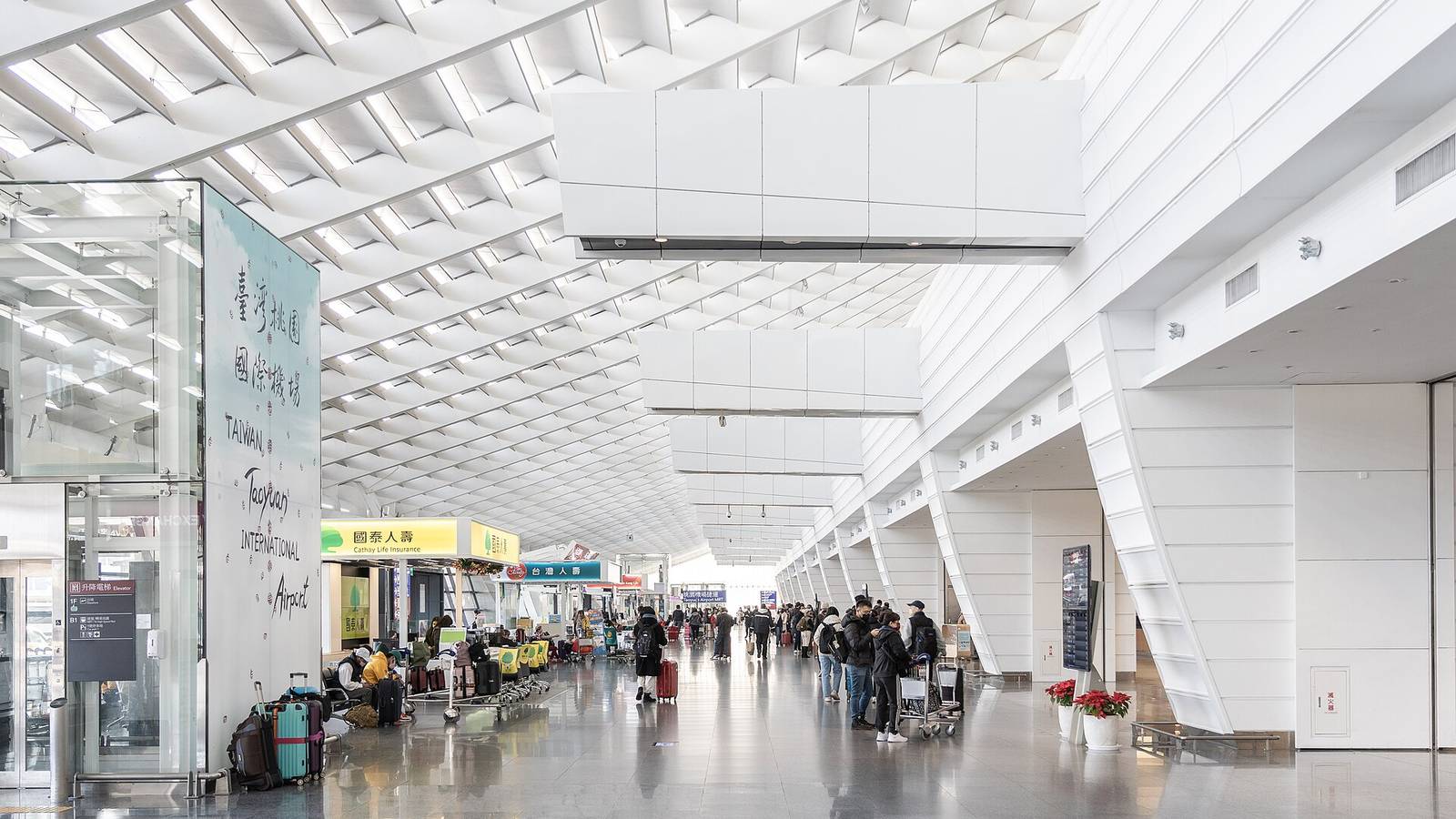Travelers push luggage through the departures hall of Terminal 1 at Taoyuan Airport beneath a white grid ceiling
