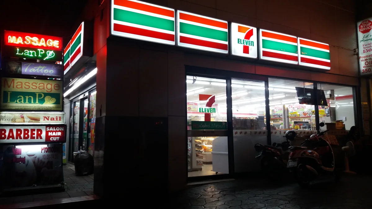 夜のバンコク・スクンビット通りで赤と緑の看板が光る7-Elevenと、店先に止まったバイク