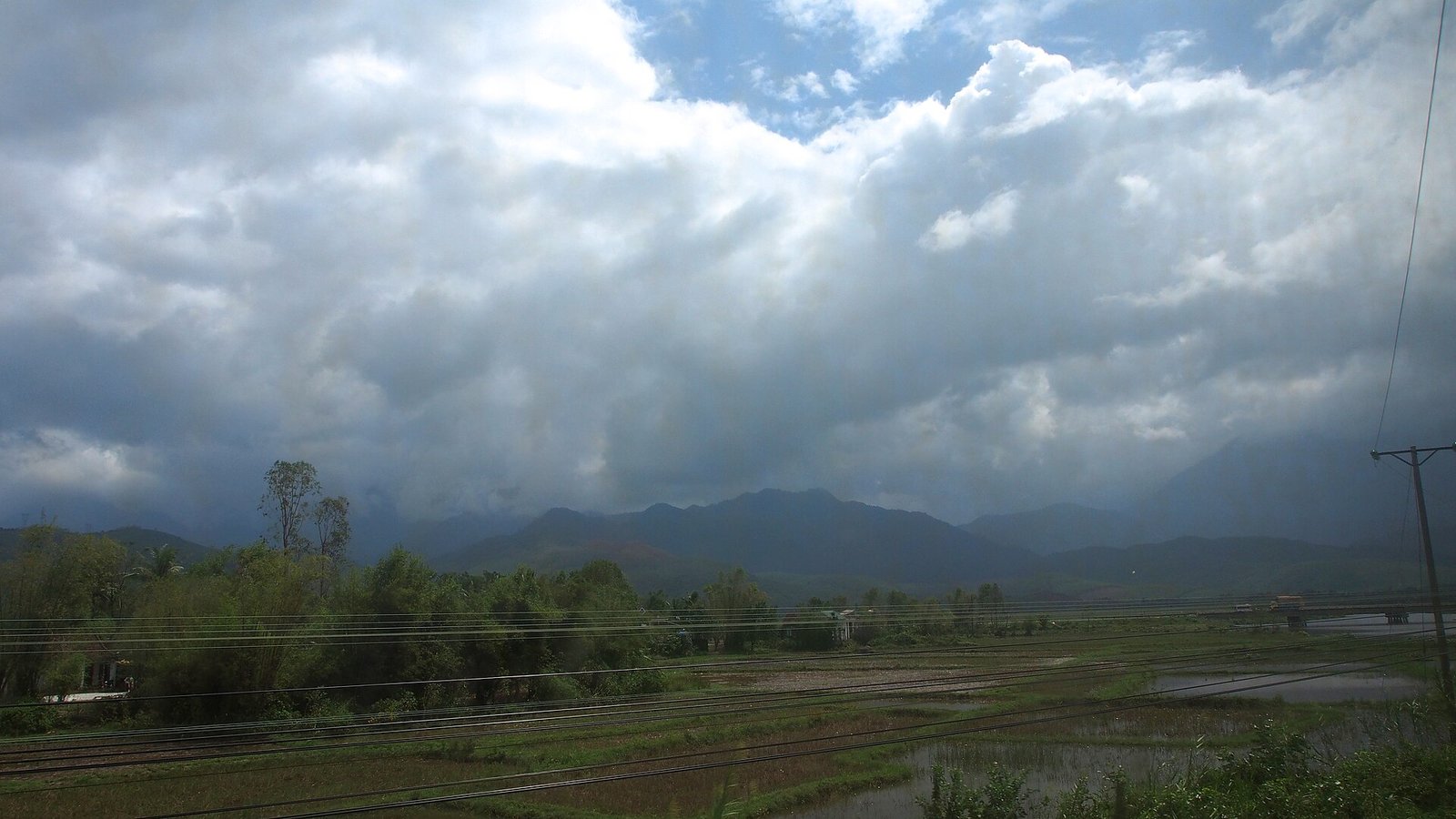 越南中部海雲嶺一帶的統一鐵路，前景是並排的軌道，遠方是雲層低壓的山脈與水田