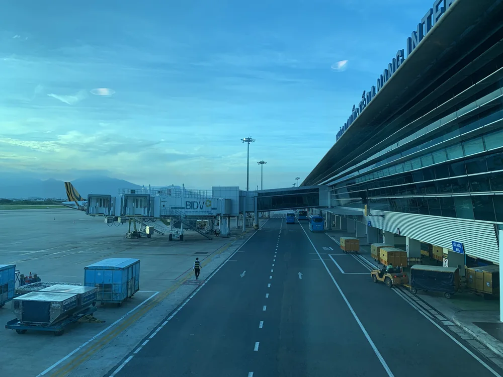 傍晚的峴港國際機場國際線航廈，外牆上方有峴港國際機場字樣，旁邊是登機橋、機坪巴士與行李拖車
