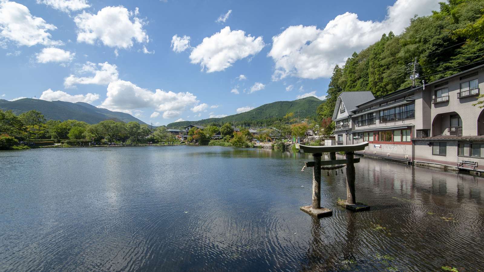 由布院金鱗湖：晴天下的湖面、立在湖中的石鳥居與岸邊的建築，遠景是由布院四周的山